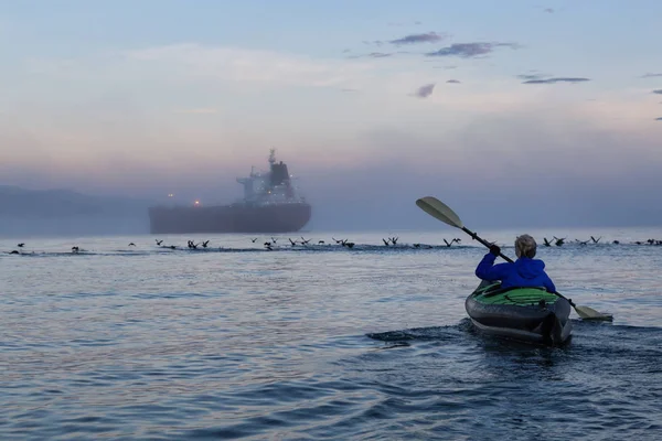 Adventure girl is kayaking on an inflatable kayak in Horseshoe Bay with a ship in the background. Taken in Vancouver, BC, Canada, during a winter sunset.