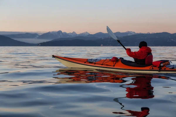 Adventure Man on a Sea Kayak is kayaking during a vibrant and colorful winter sunset. Taken in Vancouver, British Columbia, Canada. Adventure, Vacation Concept