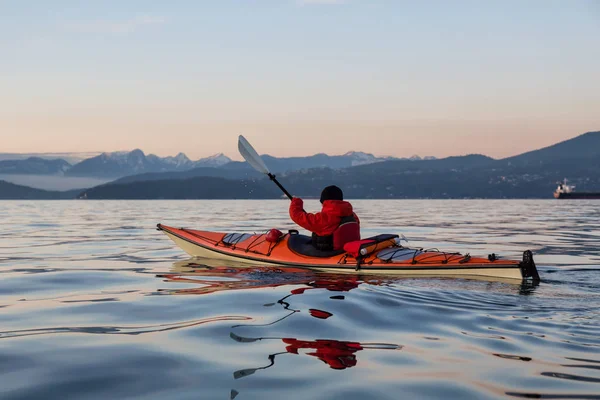 Adventure Man on a Sea Kayak is kayaking during a vibrant and colorful winter sunset. Taken in Vancouver, British Columbia, Canada. Adventure, Vacation Concept