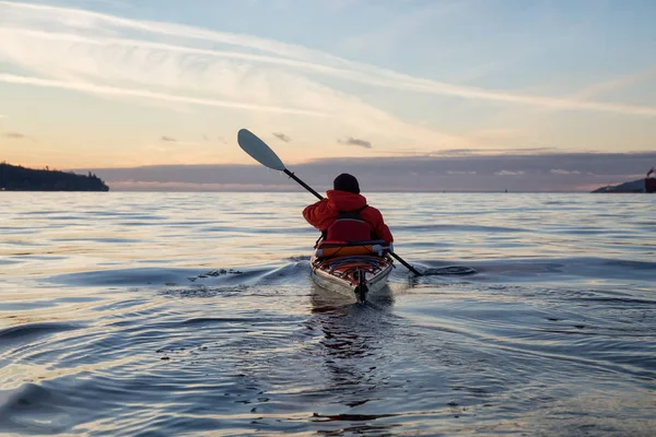 Adventure Man on a Sea Kayak is kayaking during a vibrant and colorful winter sunset. Taken in Vancouver, British Columbia, Canada. Adventure, Vacation Concept