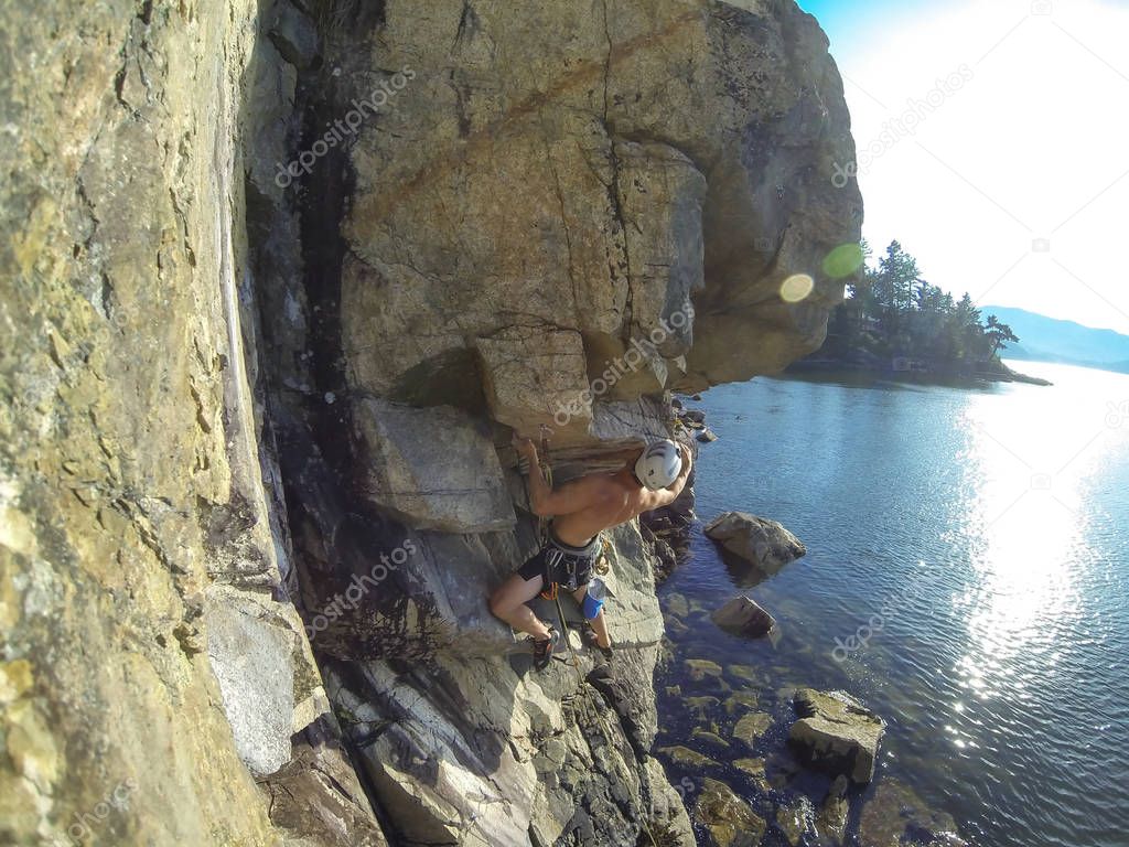 Man Rock Climbing a steep rockface during a bright summer day. Taken in Copper Cover, Horseshoe Bay, West Vancouver, British Columbia, Canada.
