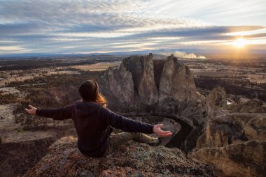 Bir uçurumun üstünde Kollarını açarak canlı bir gün batımı sırasında oturan maceracı adam. Smith Rock, Oregon, Amerika'nın alınan. Konsept: Macera, özgürlük, seyahat, tatil, tatil