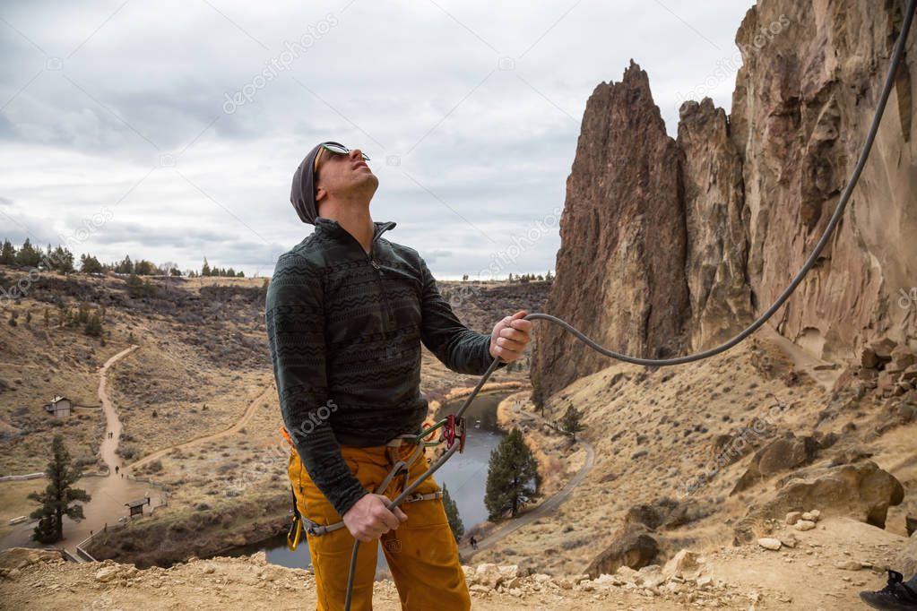Adventurous man is belaying his partner while rock climbing. Taken in Smith Rock, Oregon, North America.