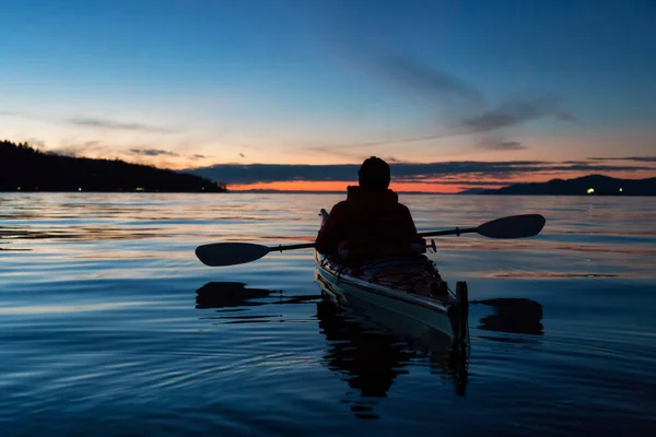 Man Kayaking on a sea kayak during a vibrant sunset. Taken near Jericho Beach, Vancouver, British Columbia, Canada.