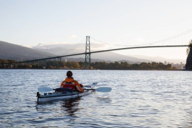 Sea Kayaking around Lions Gate Bridge and Stanley Park during a bright and vibrant morning. Taken in Vancouver, British Columbia, Canada. clipart