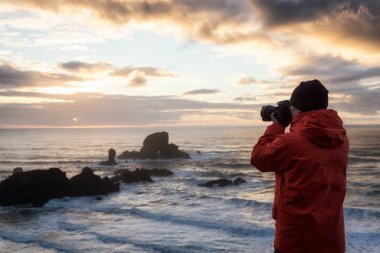 Photographer with a camera is taking pictures during a vibrant and colorful winter sunset. Taken in Ecola State Park near Canon Beach, Oregon Coast, United States of America.