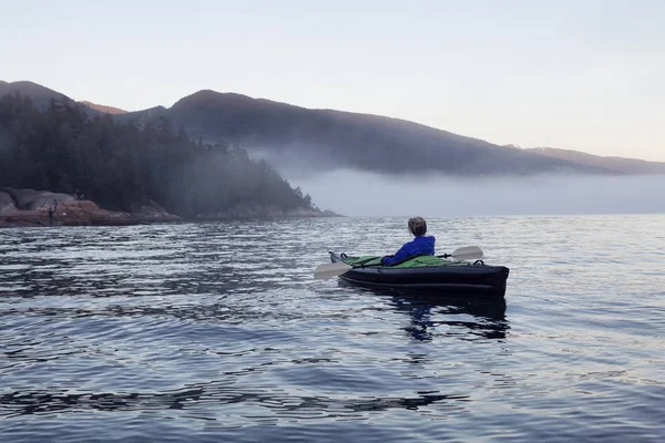 Adventurous woman is sea kayaking on an inflatable kayak during a vibrant winter sunset. Taken in Horseshoe Bay, West Vancouver, BC, Canada. Concept: adventure, holiday, vacation, explore