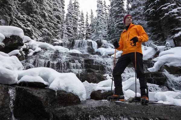 Adventure mNan standing besides a beautiful waterfall in the winter wilderness. Taken in Joffre Lakes, North of Vancouver, British Columbia, Canada. Concept: Adventure, holiday