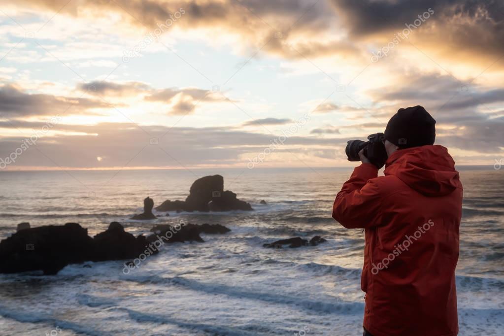 Photographer with a camera is taking pictures during a vibrant and colorful winter sunset. Taken in Ecola State Park near Canon Beach, Oregon Coast, United States of America.