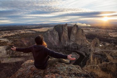 Bir uçurumun üstünde Kollarını açarak canlı bir gün batımı sırasında oturan maceracı adam. Smith Rock, Oregon, Amerika'nın alınan. Konsept: Macera, özgürlük, seyahat, tatil, tatil