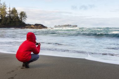 Woman in a bright red jacket is enjoying the beautiful scenery of the sandy beach on Pacific Ocean Coast. Taken near Tofino, Vancouver Island, BC, Canada. clipart