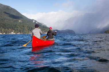 Ahşap bir Kano üzerinde çift arkadaşlar Kanada dağlarla çevrili bir giriş kürek çekmeye. Hint kol, Deep Cove yakınındaki kuzey Vancouver, British Columbia, Kanada çekilmiş.