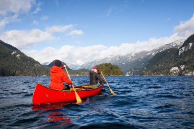 Ahşap bir Kano üzerinde çift arkadaşlar Kanada dağlarla çevrili bir giriş kürek çekmeye. Hint kol, Deep Cove yakınındaki kuzey Vancouver, British Columbia, Kanada çekilmiş.