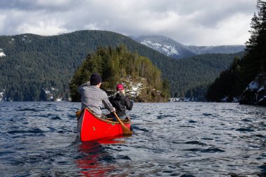 Ahşap bir Kano üzerinde çift arkadaşlar Kanada dağlarla çevrili bir giriş kürek çekmeye. Hint kol, Deep Cove yakınındaki kuzey Vancouver, British Columbia, Kanada çekilmiş.