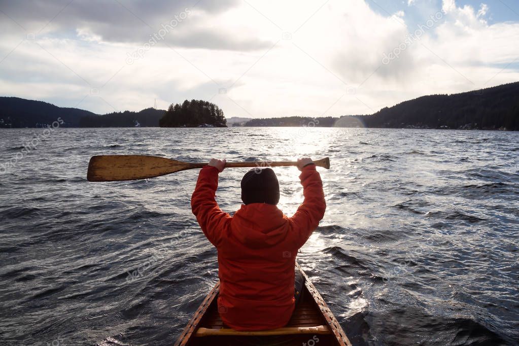 Man on a wooden canoe is holding his paddle up in the air. Taken in Indian Arm, North of Vancouver, British Columbia, Canada.