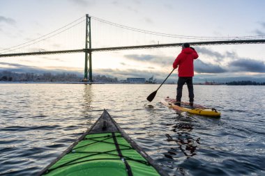 Maceracı adam Standup kürek tahtası Lions Gate Köprüsü canlı kış gün doğumu sırasında doldurma. Vancouver, British Columbia, Kanada alınan.