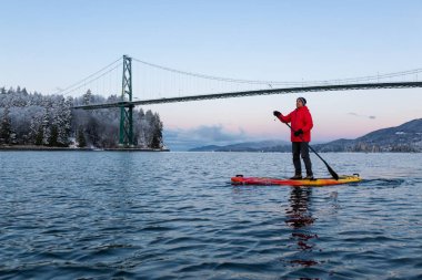 Maceracı adam Standup kürek tahtası Lions Gate Köprüsü canlı kış gün doğumu sırasında doldurma. Vancouver, British Columbia, Kanada alınan.