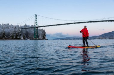 Maceracı adam Standup kürek tahtası Lions Gate Köprüsü canlı kış gün doğumu sırasında doldurma. Vancouver, British Columbia, Kanada alınan.