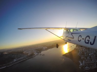 Vancouver, British Columbia, Kanada - 22 Şubat 2018: Küçük uçak, Cessna 172, canlı bir gün batımı sırasında şehrin üzerinde uçuyor.