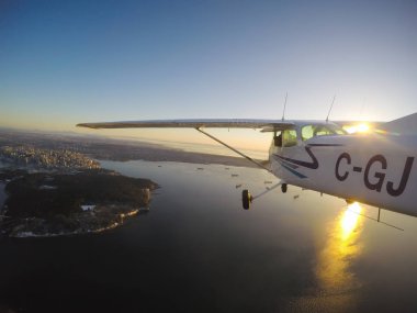 Vancouver, British Columbia, Kanada - 22 Şubat 2018: Küçük uçak, Cessna 172, canlı bir gün batımı sırasında şehrin üzerinde uçuyor.