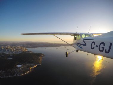 Vancouver, British Columbia, Kanada - 22 Şubat 2018: Küçük uçak, Cessna 172, canlı bir gün batımı sırasında şehrin üzerinde uçuyor.