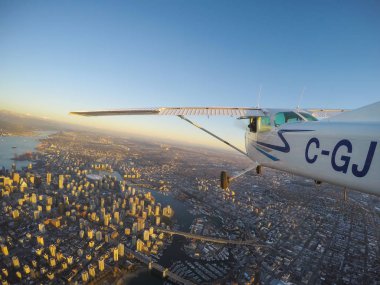 Vancouver, British Columbia, Kanada - 22 Şubat 2018: Küçük uçak, Cessna 172, canlı bir gün batımı sırasında şehrin üzerinde uçuyor.