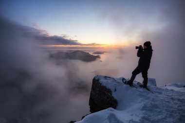 Sarp bir uçurum kenarında maceracı adam canlı bir gün batımı sırasında güzel manzara resimleri alıyor. Üstünde tepe-in St Mark's Peak, Kuzey Vancouver, Bc, Kanada alınan.