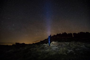 Night scene of a rugged mountain landscape with the sky full of stars and a man standing with headlamp. Taken in Frenchman Coulee, Vantage, Washington, USA. clipart