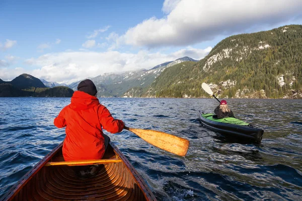 Man canoeing and woman kayaking during a windy winter day. Taken in Indian Arm, Deep Cove, Vancouver, BC, Canada. Concept: adventure, holiday, vacation