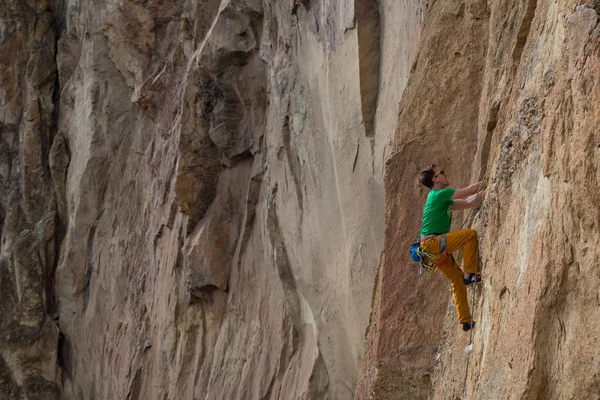 stock image Adventurous man is rock climbing on the side of a steep cliff during a cloudy winter evening. Taken in Smith Rock, Oregon, North America.