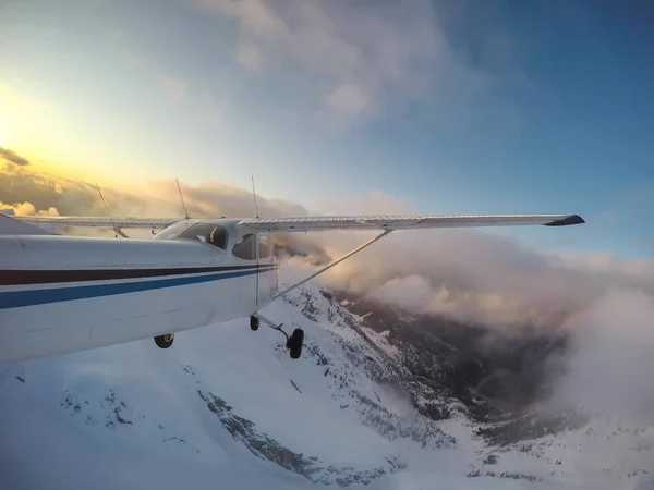 Small airplane flying overtop of the beautiful Canadian Mountain Landscape during a vibrant sunset. Taken North of Vancouver, British Columbia, Canada.