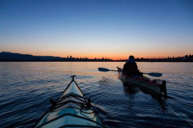 Arka planda şehir manzarası ile maceracı kız Deniz kanosu canlı kış gün doğumu sırasında. Şehir merkezinde alınan Vancouver, British Columbia, Kanada.