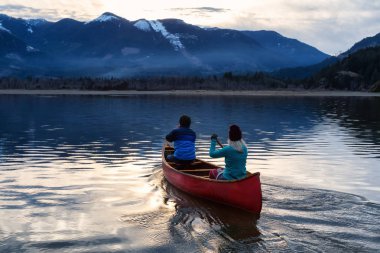Ahşap bir Kano üzerinde maceracı insanlar sırasında canlı bir günbatımı güzel Kanada dağ manzarası tadını çıkarıyor. Harrison nehir, Vancouver, British Columbia, Kanada doğusunda alınan.