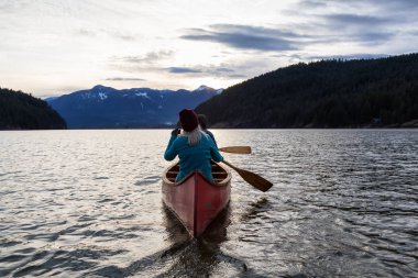Ahşap bir Kano üzerinde maceracı insanlar sırasında canlı bir günbatımı güzel Kanada dağ manzarası tadını çıkarıyor. Harrison nehir, Vancouver, British Columbia, Kanada doğusunda alınan.