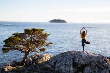 Genç kadın canlı bir gün batımı sırasında pratik Yoga bir kayalık ada üzerinde. Whytecliff Park, Horseshoe Bay, Batı Vancouver, British Columbia, Kanada alınan.