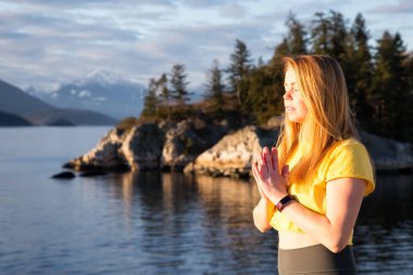 Genç kadın canlı bir gün batımı sırasında pratik Yoga bir kayalık ada üzerinde. Whytecliff Park, Horseshoe Bay, Batı Vancouver, British Columbia, Kanada alınan.