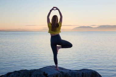Genç kadın canlı bir gün batımı sırasında pratik Yoga bir kayalık ada üzerinde. Whytecliff Park, Horseshoe Bay, Batı Vancouver, British Columbia, Kanada alınan.