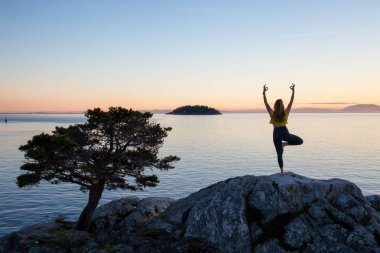 Genç kadın canlı bir gün batımı sırasında pratik Yoga bir kayalık ada üzerinde. Whytecliff Park, Horseshoe Bay, Batı Vancouver, British Columbia, Kanada alınan.