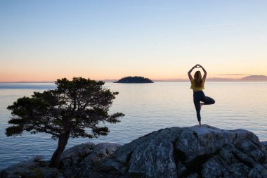 Genç kadın canlı bir gün batımı sırasında pratik Yoga bir kayalık ada üzerinde. Whytecliff Park, Horseshoe Bay, Batı Vancouver, British Columbia, Kanada alınan.