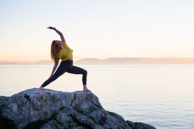 Genç kadın canlı bir gün batımı sırasında pratik Yoga bir kayalık ada üzerinde. Whytecliff Park, Horseshoe Bay, Batı Vancouver, British Columbia, Kanada alınan.