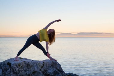 Genç kadın canlı bir gün batımı sırasında pratik Yoga bir kayalık ada üzerinde. Whytecliff Park, Horseshoe Bay, Batı Vancouver, British Columbia, Kanada alınan.