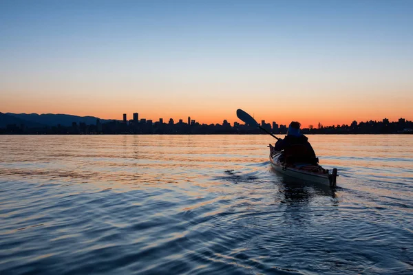 Arka planda şehir manzarası ile maceracı kız Deniz kanosu canlı kış gün doğumu sırasında. Şehir merkezinde alınan Vancouver, British Columbia, Kanada.