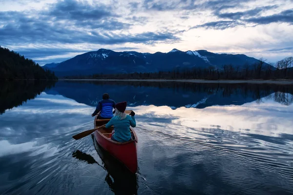 Adventurous people on a wooden canoe are enjoying the beautiful Canadian Mountain Landscape during a vibrant sunset. Taken in Harrison River, East of Vancouver, British Columbia, Canada.