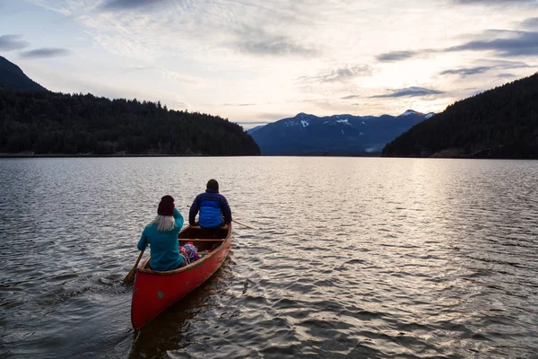 Adventurous people on a wooden canoe are enjoying the beautiful Canadian Mountain Landscape during a vibrant sunset. Taken in Harrison River, East of Vancouver, British Columbia, Canada.