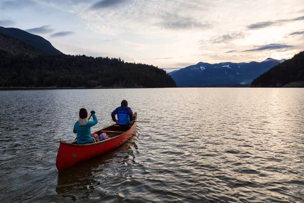 Adventurous people on a wooden canoe are enjoying the beautiful Canadian Mountain Landscape during a vibrant sunset. Taken in Harrison River, East of Vancouver, British Columbia, Canada.