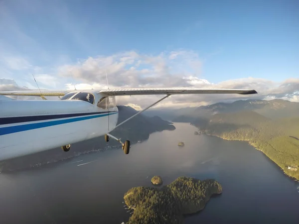 Small airplane flying over Deep Cove during a vibrant sunset. Taken in Vancouver, British Columbia, Canada.