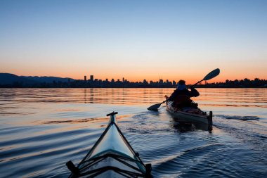 Arka planda şehir manzarası ile maceracı kız Deniz kanosu canlı kış gün doğumu sırasında. Şehir merkezinde alınan Vancouver, British Columbia, Kanada.