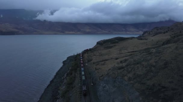 空中ドローン曲線鉄道 曇り秋の日の出の間に湖近くの列車のパノラマの景観 ブリティッシュ コロンビア州 カナダのインテリアは — ストック動画