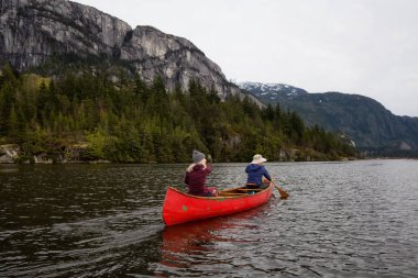 Ahşap bir Kano üzerinde maceracı insanlar bir nehirde güzel kayalık dağ içinde belgili tanımlık geçmiş ile kürek çekmeye. Squamish, Vancouver, Bc, Kanada kuzeyindeki alınan.