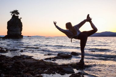 Pratik yoga bir kayalık kıyısında canlı bir gün batımı sırasında bir genç kadın. Stanley Park, Vancouver, British Columbia, Kanada alınan.
